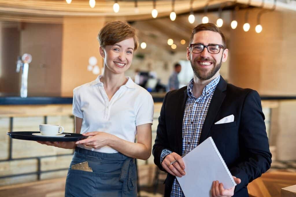 Group portrait of cheerful bearded restaurant manager and server posing for photography while standing against bar counter