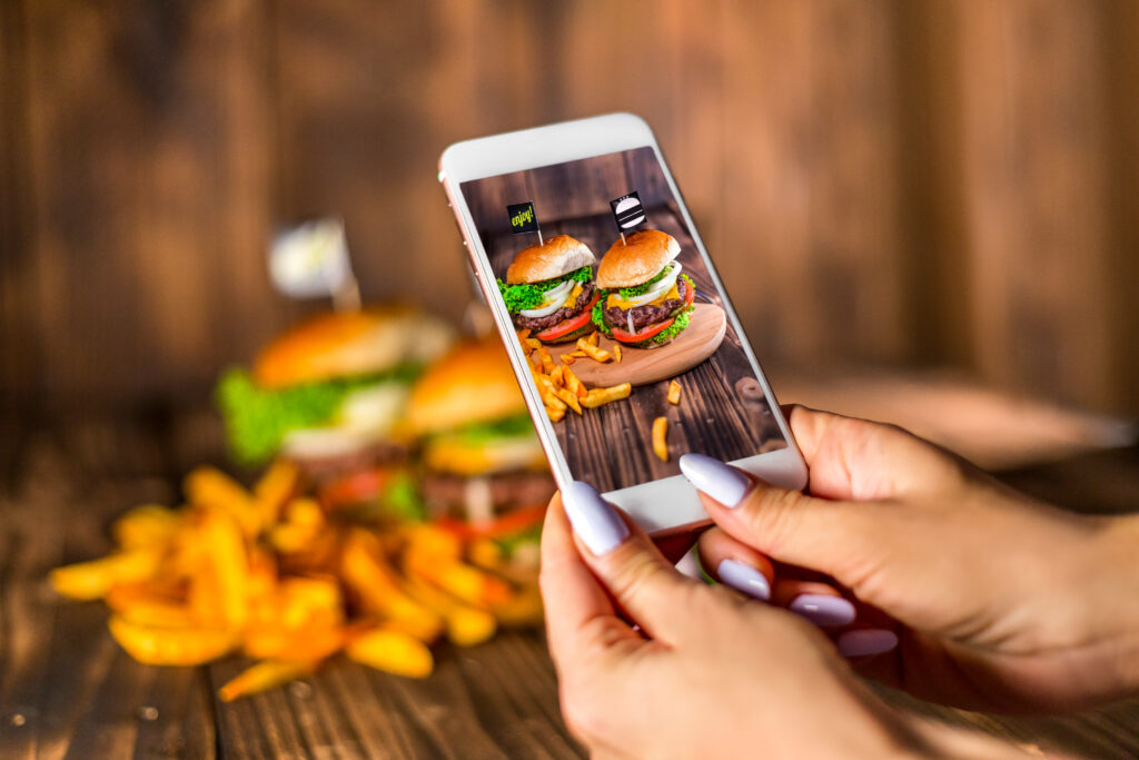 Social media marketing for restaurants: Person holding a smartphone, taking a photo of a burger and fries